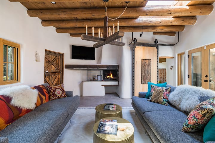Santa Fe adobe rental with exposed log beam ceiling, kiva fireplace, and colorful Southwestern decor