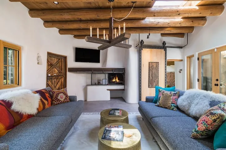 Santa Fe adobe rental with exposed log beam ceiling, kiva fireplace, and colorful Southwestern decor