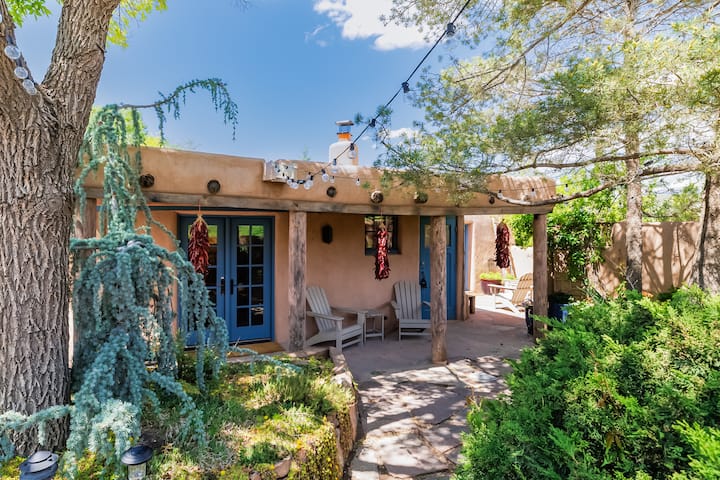 Adobe casita exterior with covered portal, string lights, Adirondack chairs, and hanging ristras